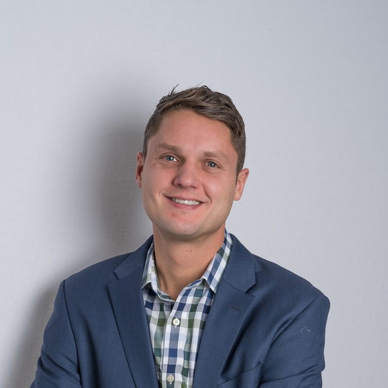 stokes-headshot headshot of smiling man in blue jacket and blue and white checked shirt