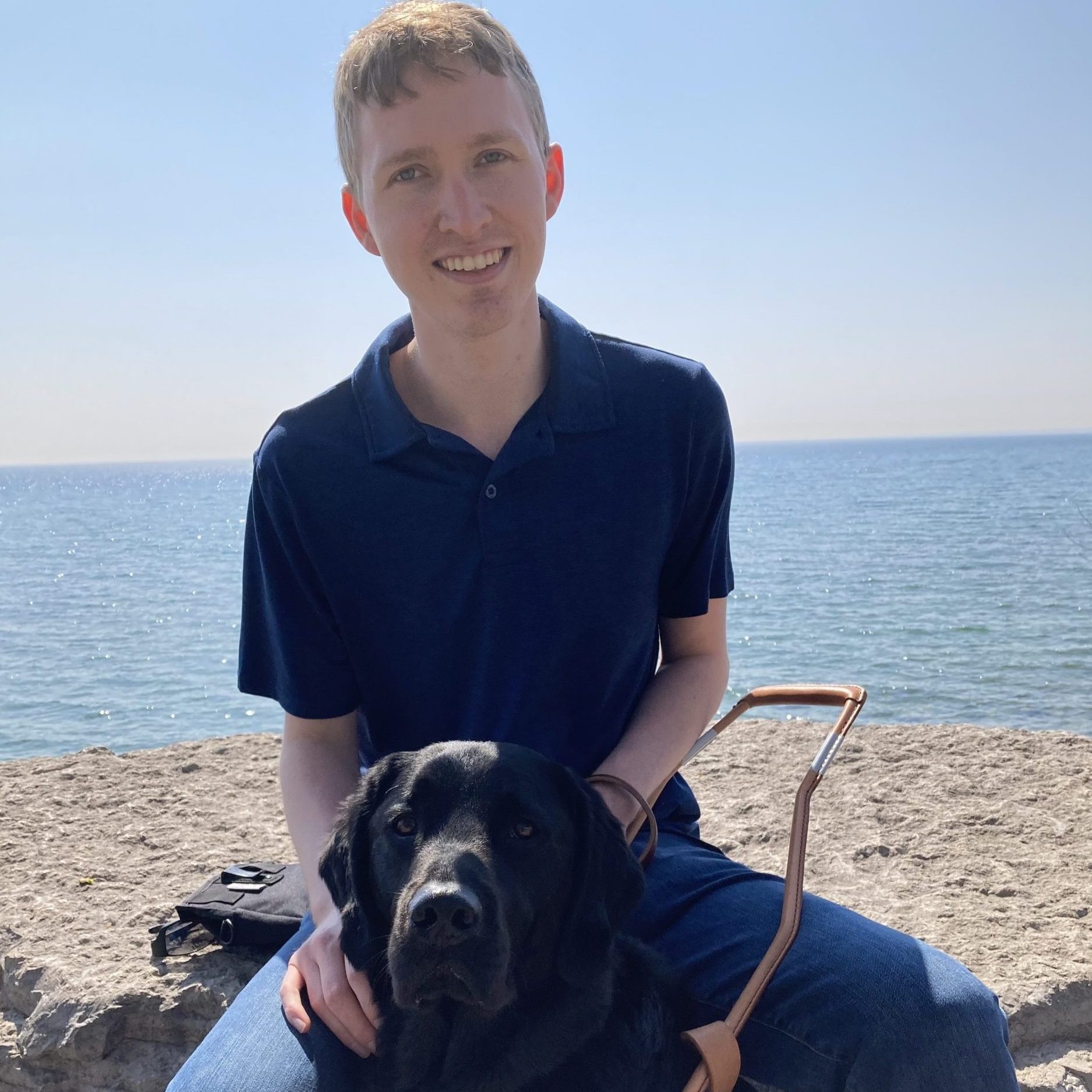baloo-and-jack Young man sits with black dog at beach